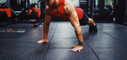 man in red tank top and black shorts doing push up on the street