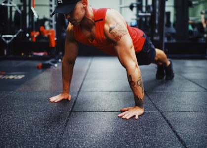 man in red tank top and black shorts doing push up on the street